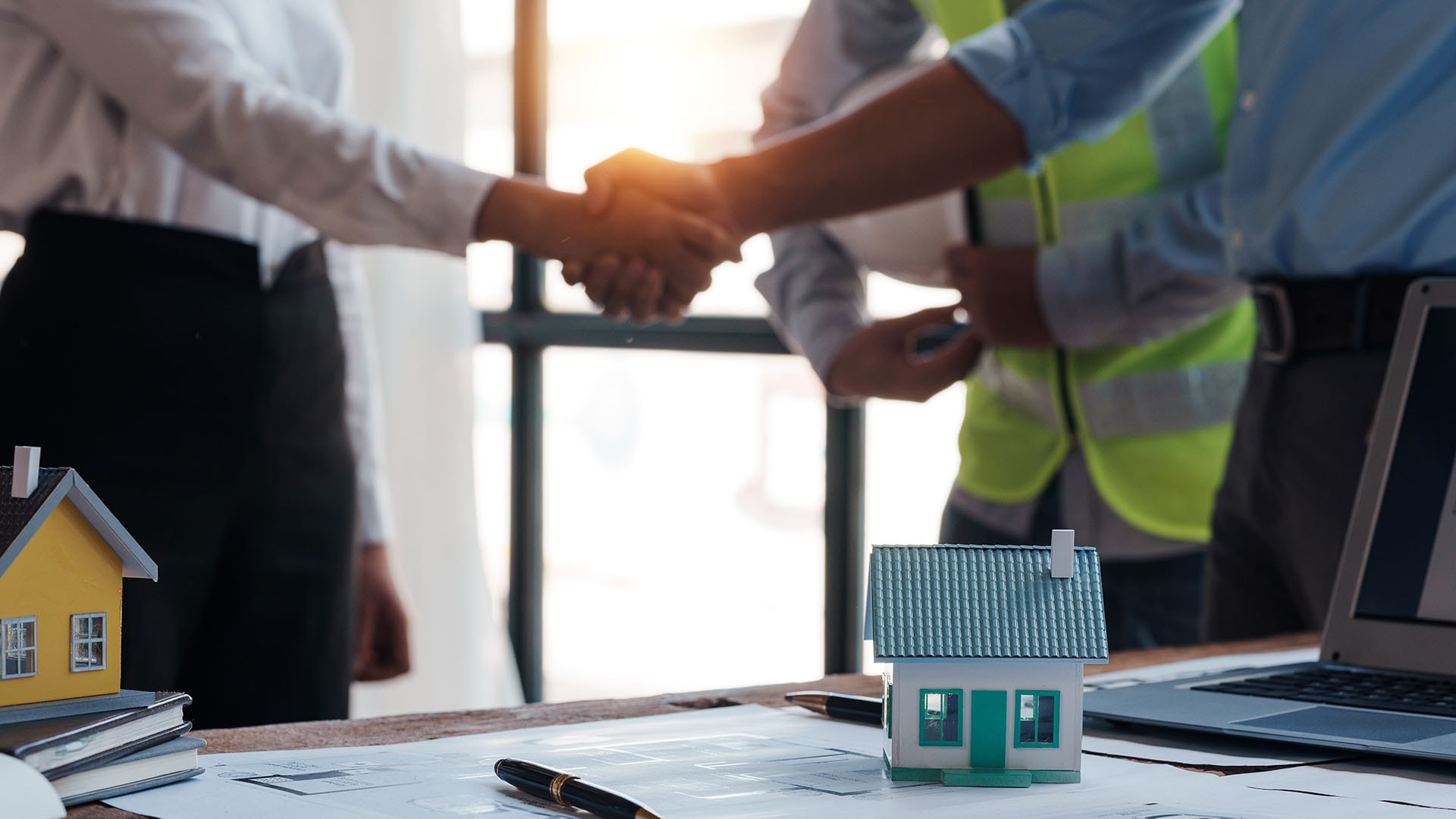 1920 arkkitehti ja insinööri kättelevät taustalla mies keltaisessa huomioliivissä