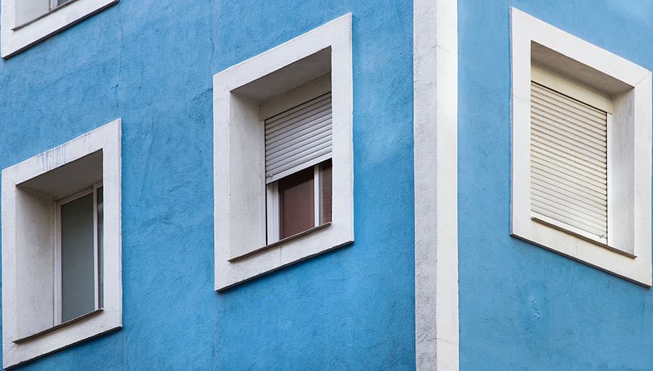 1920 vaaleansinisellä värillä maalattu rapatun kerrostalon kulmaa, jossa valkoisella maalilla maalatut ikkunanpielet Smartvatten shutterstock_195178898