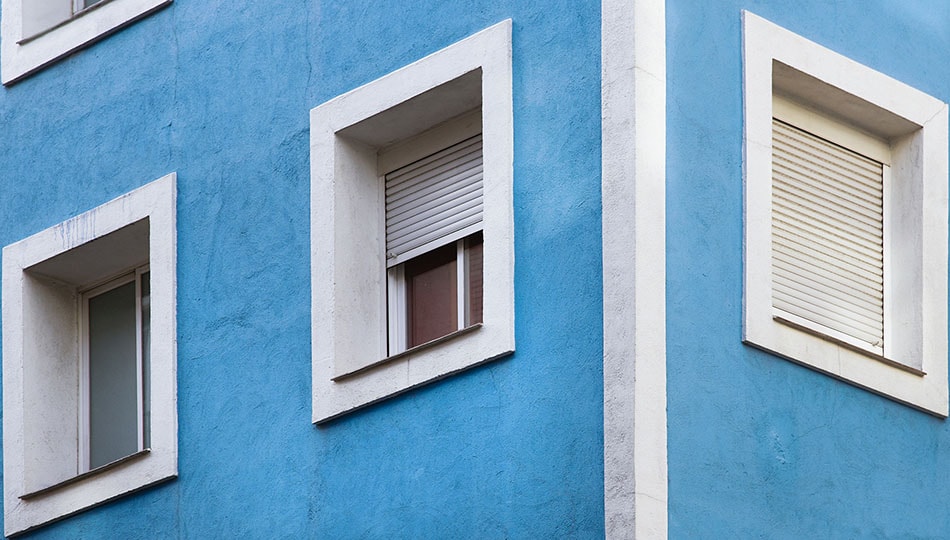 1920 vaaleansinisellä värillä maalattu rapatun kerrostalon kulmaa, jossa valkoisella maalilla maalatut ikkunanpielet Smartvatten shutterstock_195178898