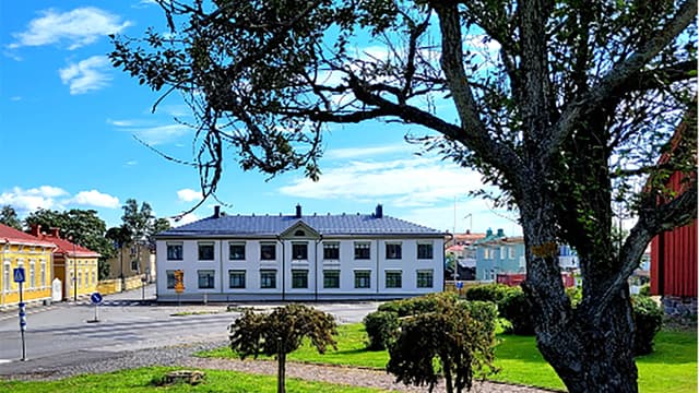 Kuvassa Kristiinan kaupungin kirkkotori. Valkoinen suuri rakennus, paljon ikkunoita, muoto 1800-luvun lopulta