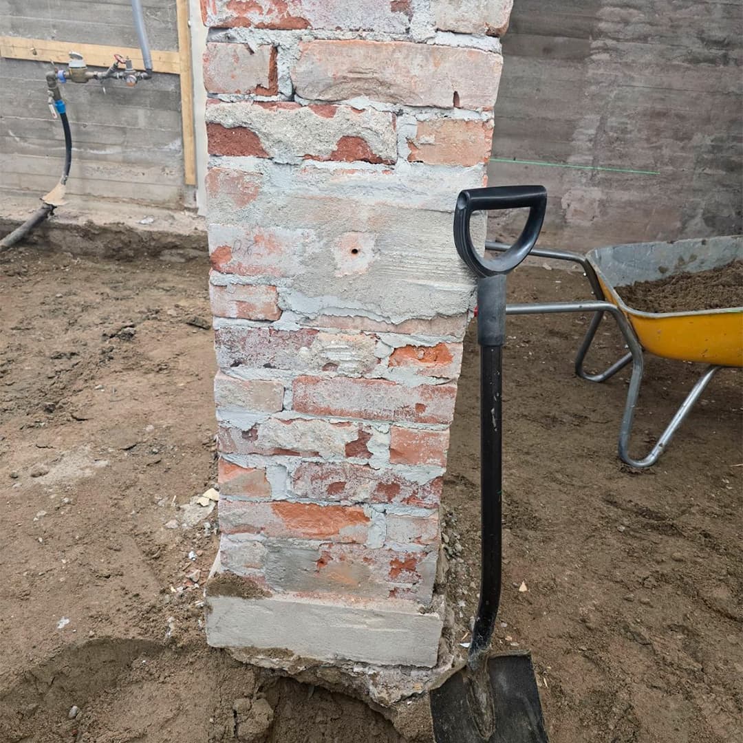 Muurattu tiilipilari keskellä lattiaa ja alustana pelkkä hiekkalattia